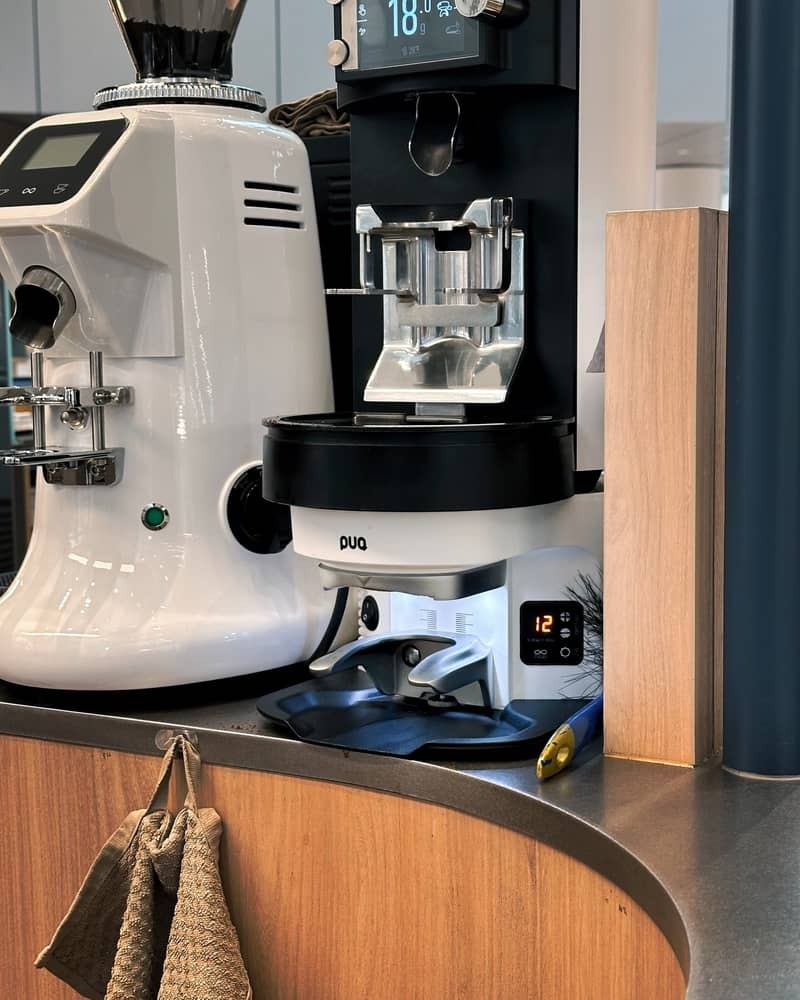 Puqpress M-Line integrated with an espresso grinder on a coffee bar.