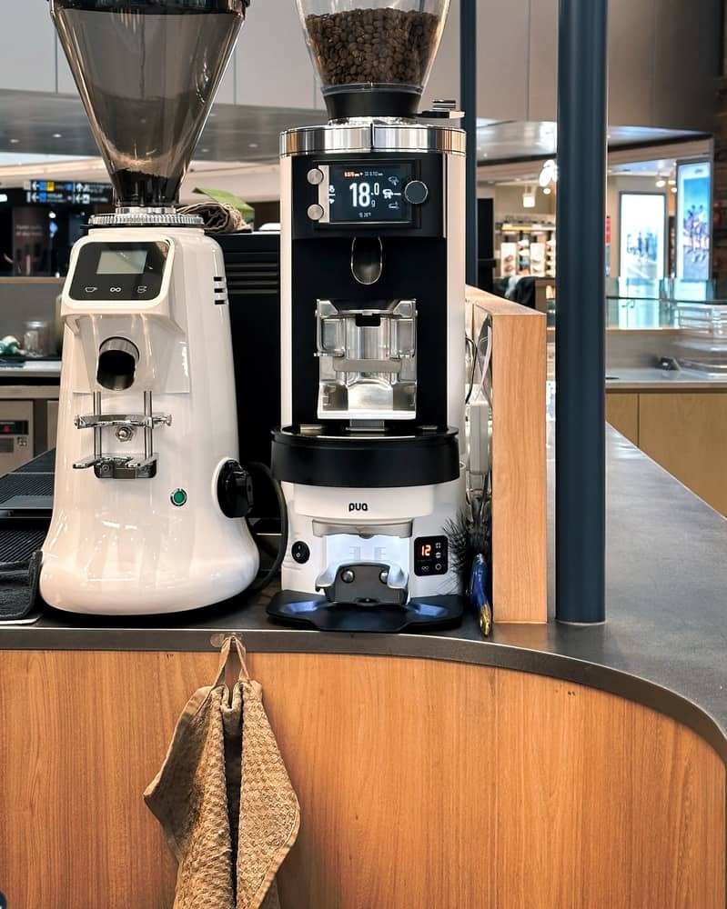 Close-up of a barista using a Puqpress M-Line integrated into a Mahlkonig grinder.